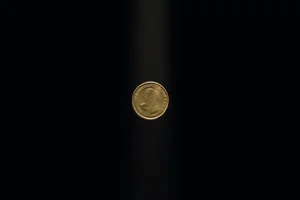 A single worn brass coin suspended in a shaft of warm light against deep black, its two faces caught between turns.