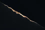 A jagged amber line of light dividing brightness from total darkness, the boundary sharp and irregular.