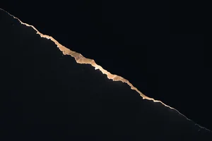 A jagged amber line of light dividing brightness from total darkness, the boundary sharp and irregular.