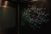 A dark control room with a wall of small green status lights on one side and a constellation of linked nodes with a single red path on the other