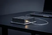 A lit miniature scale model of a data hall on a workbench, one rack glowing warm, a single cable running off toward a laptop out of frame