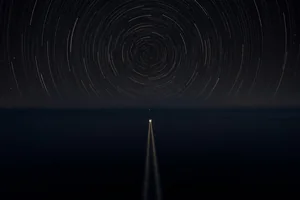 Star trails turning in closed circles over a dark sea, and below them the single straight wake of a small boat heading for the horizon