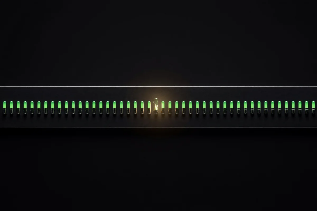 A dark instrument panel with a row of green lamps, one of them cracked and empty but still showing green