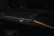 A dark studio at night: a mixing desk with one channel lit, and a small closed latch on the desk catching a warm light
