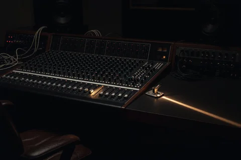 A dark studio at night: a mixing desk with one channel lit, and a small closed latch on the desk catching a warm light