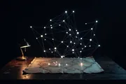 A glowing constellation of connected nodes and threads rising above a dark cartographer's map